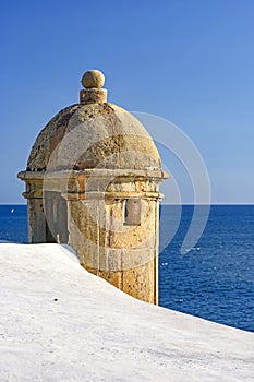 Stone guardhouse on the walls of an old colonial-style fort with the blue sea in background