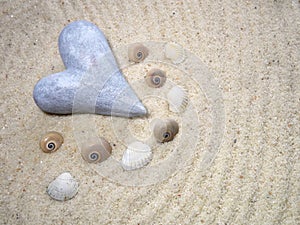 Stone heart on gray sand and shells - selective focus