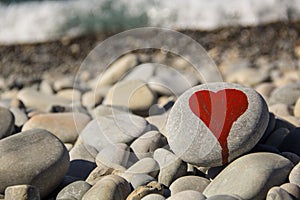 stone heart painted with a red paint marker on the pebble as a gift for Saint Valentine day on the pebble background