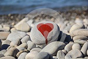 stone heart painted with a red paint marker on the pebble as a gift for Saint Valentine day on the pebble background