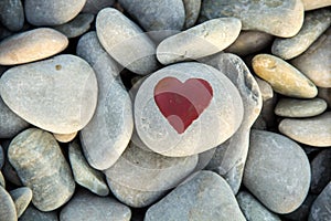 stone heart painted with a red paint marker on the pebble as a gift for Saint Valentine day on the pebble background