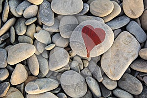 stone heart painted with a red paint marker on the pebble as a gift for Saint Valentine day on the pebble background