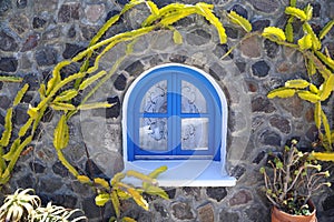 Stone house with a blue window and decorative cactus around the building in Santorini.