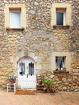 Stone house facade with windows and white wooden door and stone lintel. Stone lintel above rustic painted closed door. Rural