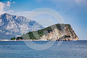 Stone island with green forest at sea near high mountain
