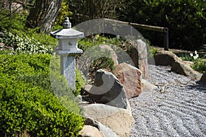 Stone lantern between evergreen plants, rocks and raked gravel,