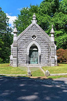 Stone mausoleum with Christian symbols and wrought-iron gate with trees in the background, at Sleepy Hollow Cemetary in Upstate