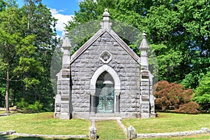 Stone mausoleum with Christian symbols and wrought-iron gate with trees in the background, at Sleepy Hollow Cemetary in Upstate