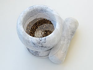 Stone mortar with ground pepper and pestle on a white kitchen table. Modern utensil made of natural marble or granite