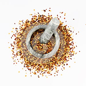Stone mortar and pestle full of crushed red cayenne pepper, dried chili flakes and seeds isolated on a white background