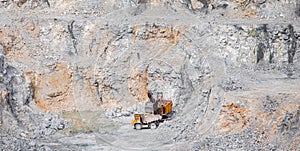 Stone open pit mine. Excavator is loading raw materials into yellow truck for transport to combine