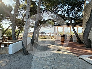 A stone path guiding the way to a beach adorned with sunbeds, surrounded by trees and crowned by a charming seaside restaurant