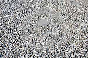 Stone paving in the square folded into circles with a larger tile in the middle of gray granite
