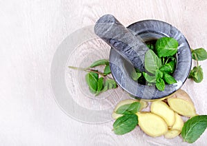 Stone pestle and mortar with mint leaves and ginger on a wooden table. top view. cold and flu remedy.