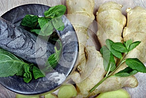 Stone pestle and mortar with mint leaves and ginger on a wooden table. top view. cold and flu remedy.