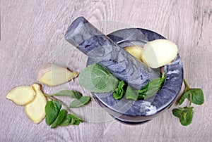 Stone pestle and mortar with mint leaves and ginger on a wooden table. top view. cold and flu remedy. copy spaces