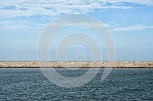 Stone Pier dividing cloudy sky and wavy sea