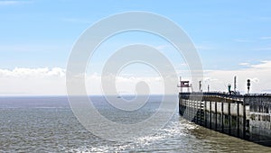 A stone pier, from which people are fishing on a beautiful summers day. There is a single sailboat on the horizon.