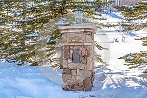 Stone post with mailbox and outdoor lamp against sunlit snow in Park City Utah