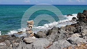 Stone pyramid on Crete rocky seashore against blue sea