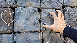 Stone Rock Bricks Behind Metal Fence With Male Hand Wall Wallpaper Background.Close Up of Male Hand Grabing Massive Stone Rocks