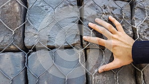 Stone Rock Bricks Behind Metal Fence With Male Hand Wall Wallpaper Background.Close Up of Massive Stone Rocks for Construction