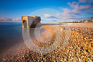 Stone and rocks beach with nobody close to a bunker and a scenic blue sky with clouds