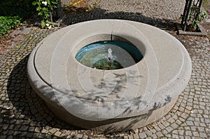 Stone sandstone circular fountain in the park. built of sandstone filled with water. lined with a light threshing gravel road with