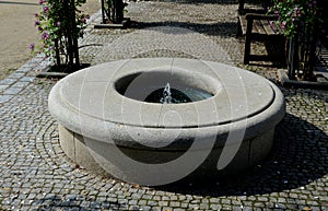 Stone sandstone circular fountain in the park. built of sandstone filled with water. lined with a light threshing gravel road with