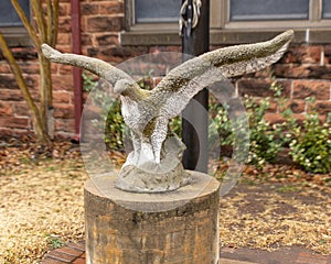Stone sculpture of an eagle with outstretched wings on a concrete pedestal at the base of a flagpole in Edmond, Oklahoma.