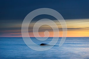 Stone in sea waves against colorful morning sky