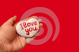 Stone in shape of heart with inscription written by hand I love you on female palm on red background