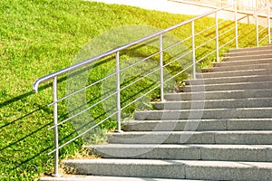 Stone staircase leading up the slope with lawn grass, with metal shining and railing.