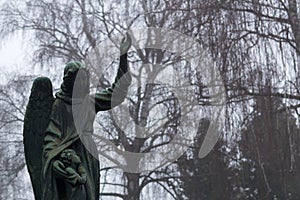 Stone statue of an angel on Cemetery during dark misty morning or night.