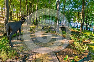 Stone statue of a deer on the square near the bridge in a green park