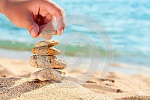 Stone tower on sand with hand.