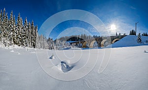 Stone viaduct arch bridge on railway through mountain snowy fir forest. Snow drifts  on wayside and hoarfrost on trees and