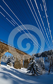 Stone viaduct arch bridge on railway through mountain snowy fir forest. Snow drifts  on wayside and hoarfrost on trees and