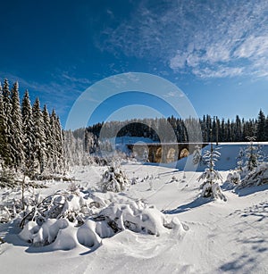 Stone viaduct arch bridge on railway through mountain snowy fir forest. Snow drifts  on wayside and hoarfrost on trees