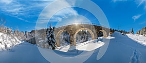 Stone viaduct on railway through mountain snowy fir forest. Snow drifts on wayside and hoarfrost on trees and