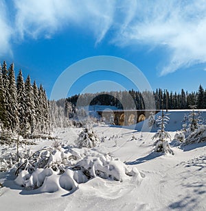 Stone viaduct on railway through mountain snowy fir forest. Snow drifts on wayside and hoarfrost on trees and