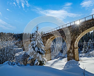 Stone viaduct on railway through mountain snowy fir forest. Snow drifts on wayside and hoarfrost on trees and