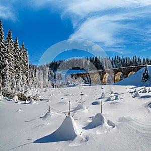 Stone viaduct on railway through mountain snowy fir forest. Snow drifts on wayside and hoarfrost on trees and