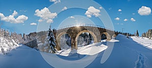 Stone viaduct on railway through mountain snowy fir forest. Snow drifts on wayside and hoarfrost on trees and