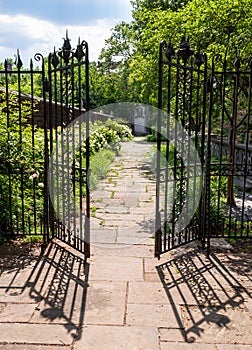 A stone walkway behind an opened wrought iron fence in a garden