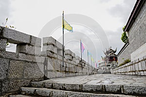 Stone wall with battlements and flags before castellated gatehouse in cloudy afternoon