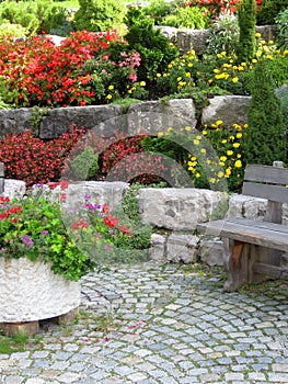 Stone wall, bench and plants on colorful landscaped garden.