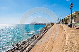 Stone wall and breakwater with blue sea and coastline of CÃ¡diz with sunlight on horizon, SPAIN photo