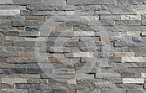 Stone wall cladding made of horizontal gray, brown and white strips of rock stacked .