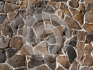 Wall made of stones of various shapes illuminated by bright sunlight. Background